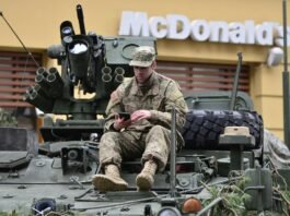 man in brown camouflage sitting on top of tank