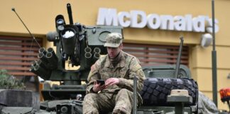 man in brown camouflage sitting on top of tank