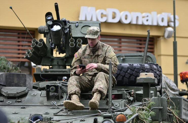 man in brown camouflage sitting on top of tank