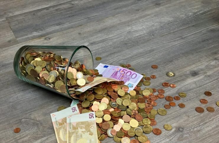 coins and banknotes scattered on gray wooden surface
