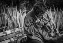 grayscale photo of man with cigarette sitting on bench