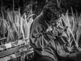 grayscale photo of man with cigarette sitting on bench