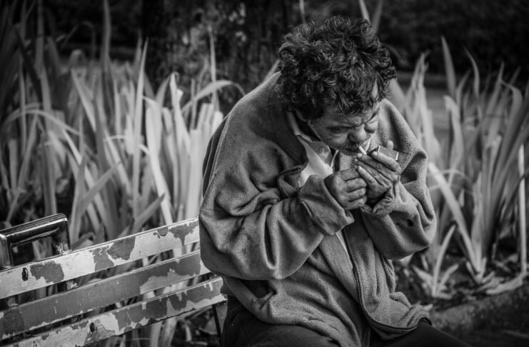 grayscale photo of man with cigarette sitting on bench
