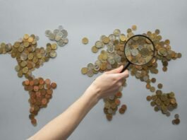 anonymous person magnifying view of coins shaped in world map