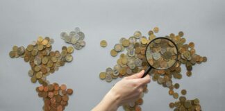 anonymous person magnifying view of coins shaped in world map