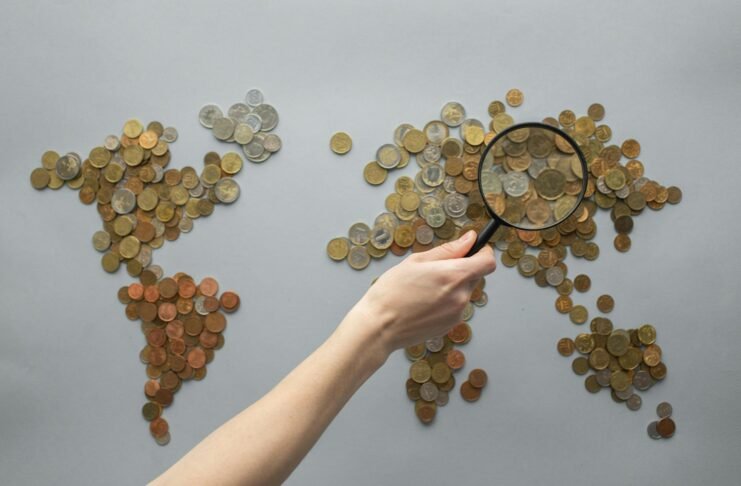 anonymous person magnifying view of coins shaped in world map